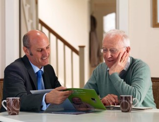 A salesman and older gentleman sitting at a table reviewing a Stannah Stairlifts brochure